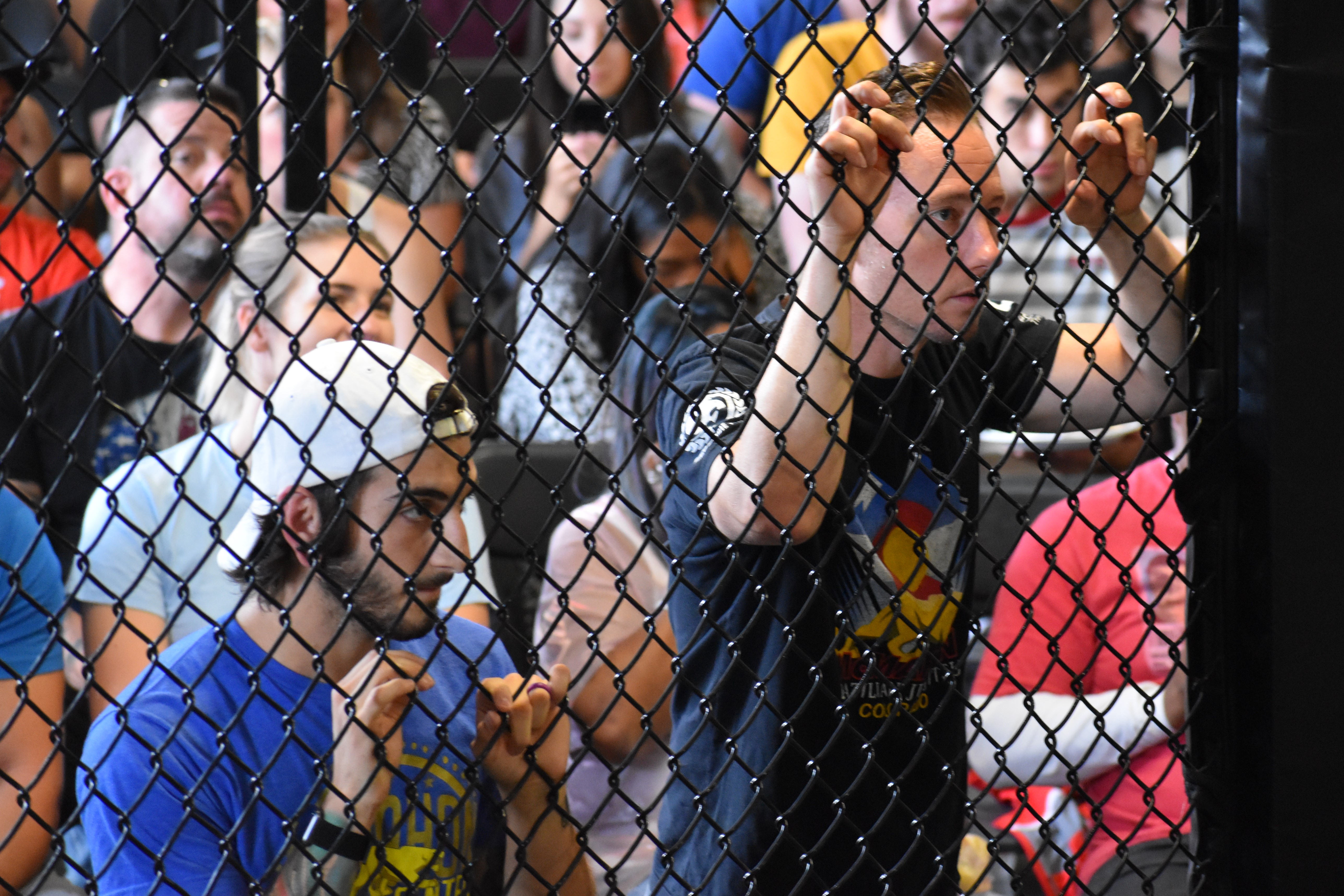 Muay-Thai-Coach-standing-outside-cage-smoker two muay thai coaches watching a fighter compete behind a MMA cage